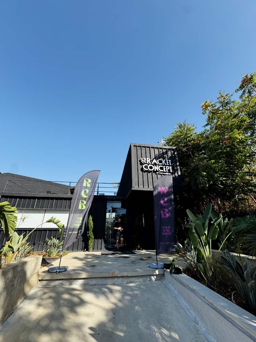 The entrance to The Racket Concept under a clear sky, Run Club Beirut and Walk Club Beirut flags either side of the door