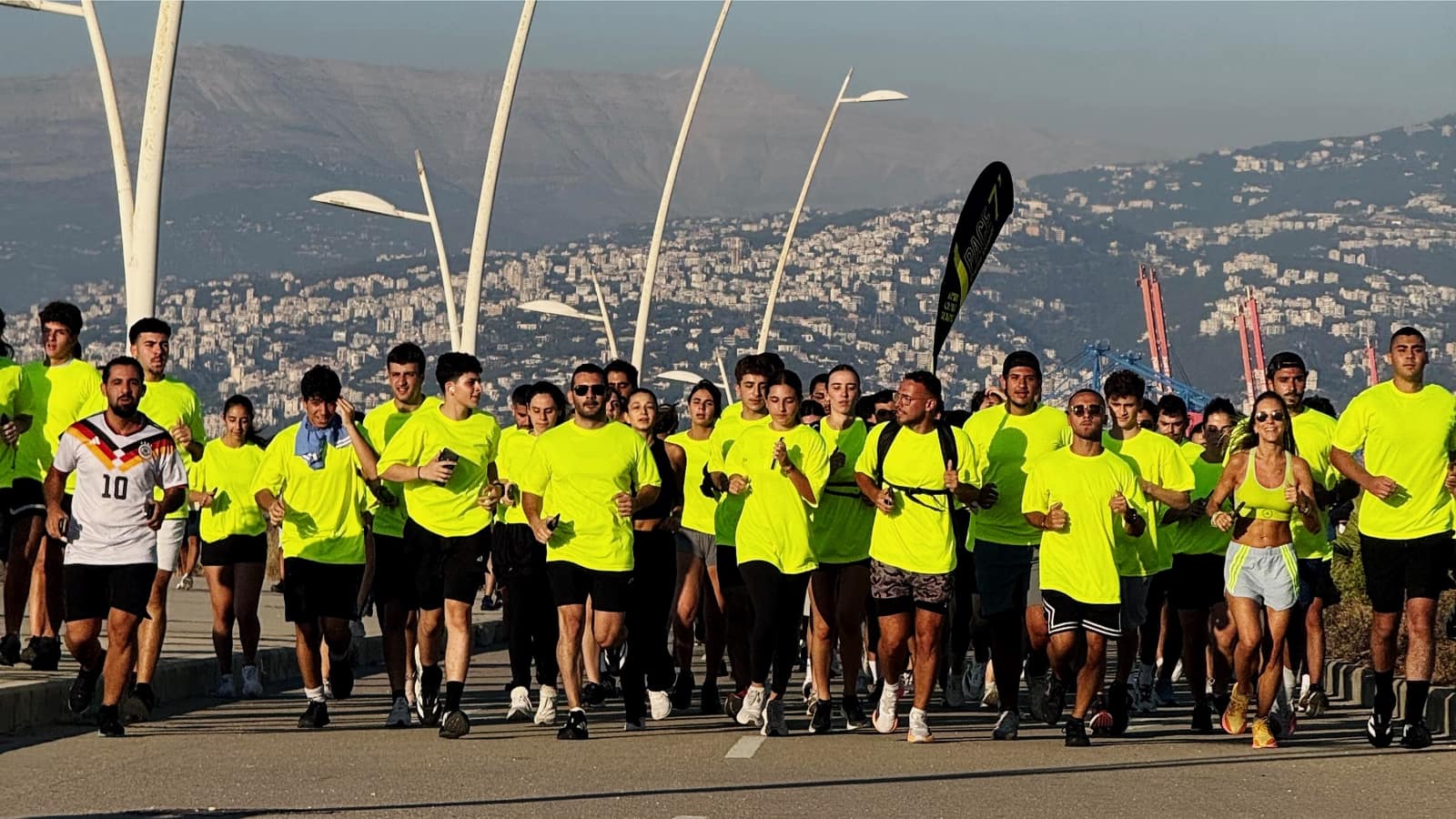 The Run Club Beirut field running the corniche in club yellow, the mountains behind them