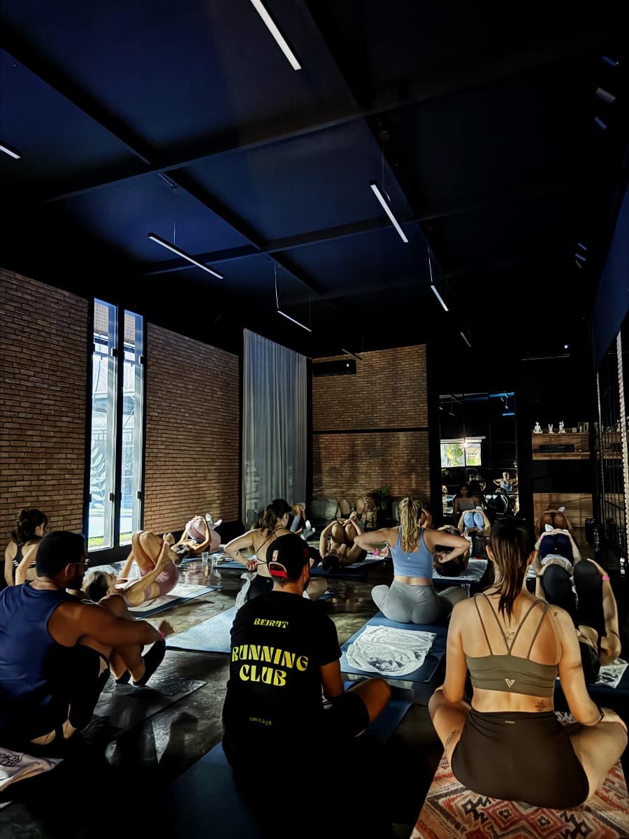A full studio of Run Club Beirut members on mats in a dark brick-walled room, a coach in a club tee sitting among them