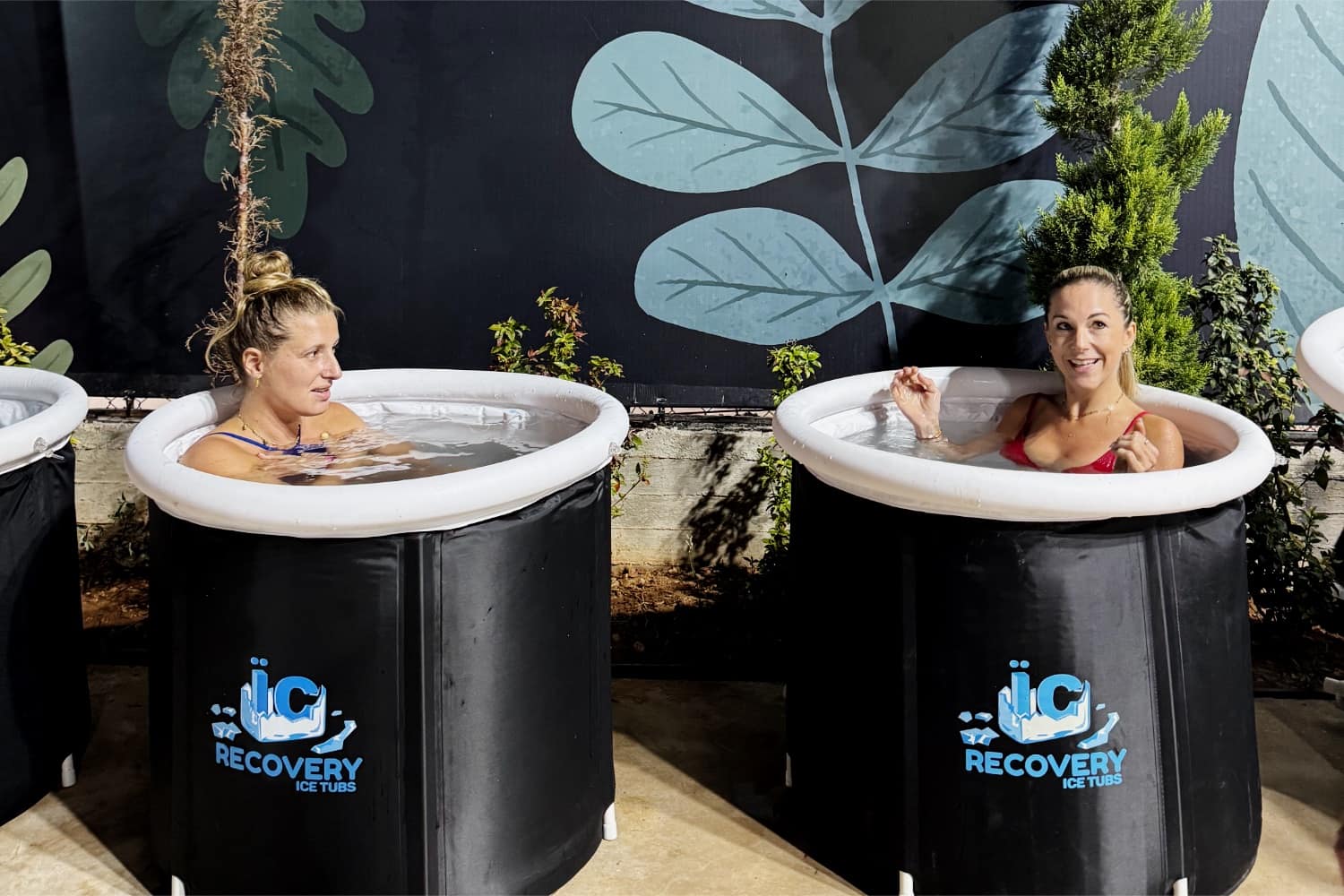 Two members sitting in ice tubs against a painted leaf backdrop at the recovery station