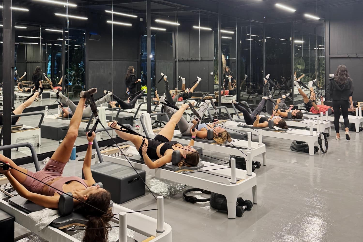 A row of reformer machines in use along a mirrored studio wall, members working through a class together