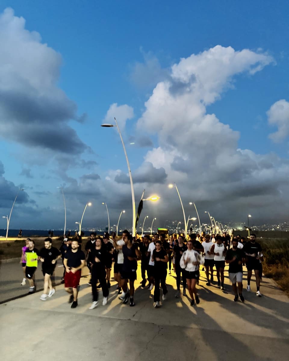 A long line of Run Club Beirut runners moving along the Beirut corniche at dusk