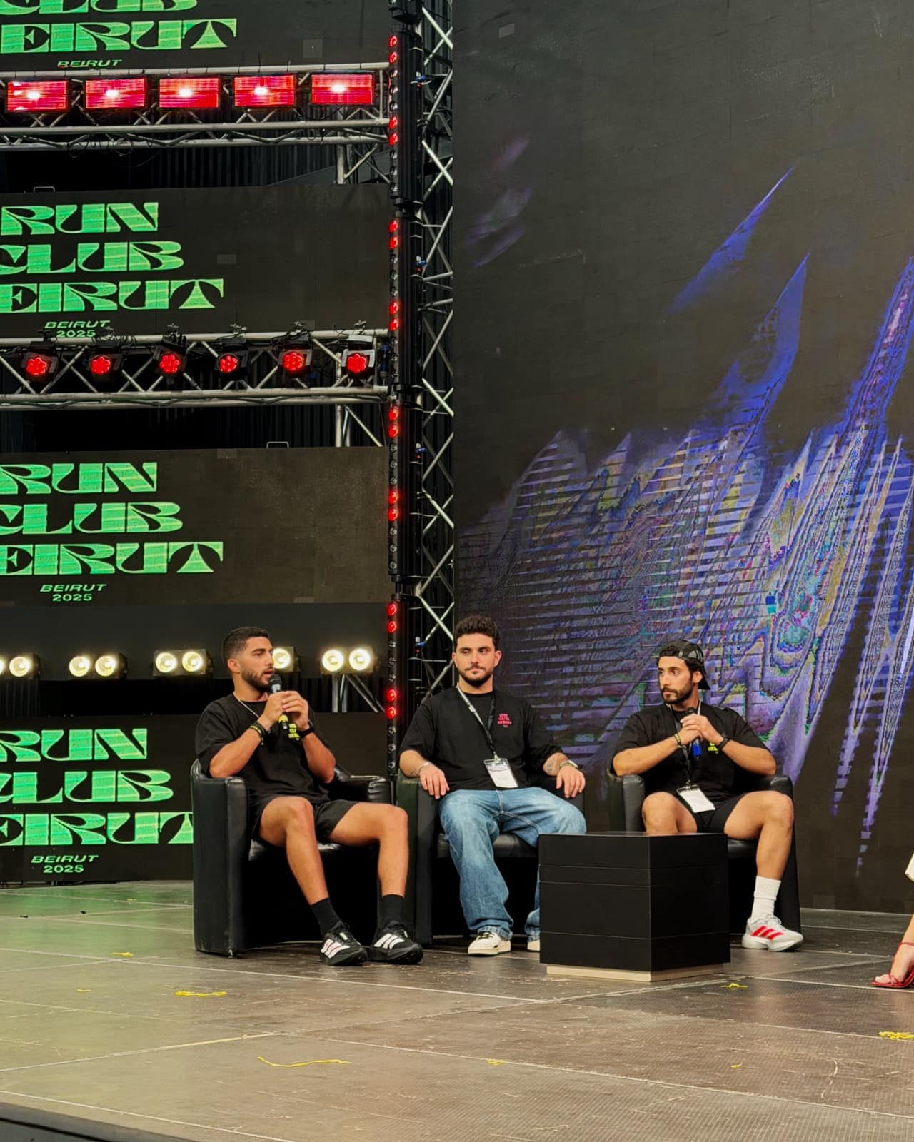 The three Run Club Beirut co-founders on stage in conversation, the club's wordmark repeating across the screens behind them